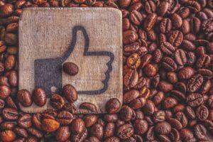 A wooden thumbs up symbol resting on a pile of roasted coffee beans, representing appreciation.